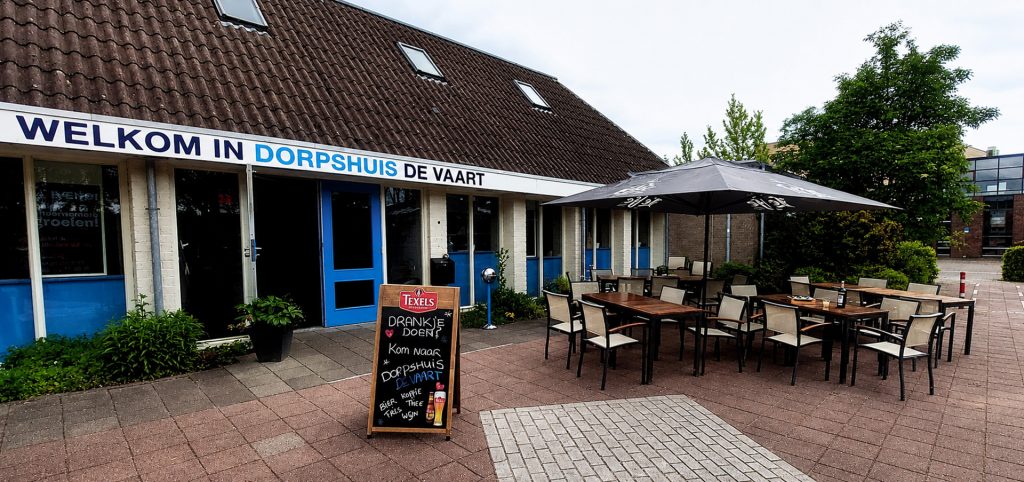 Buitenzijde van Dorpshuis De Vaart in Linschoten met terras, tafels, stoelen en welkomstbord bij de ingang.