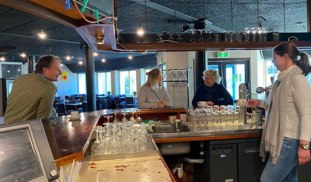 Gezellige ontmoeting aan de bar van Dorpshuis De Vaart in Linschoten, waar bezoekers met elkaar praten onder het genot van een kop koffie.